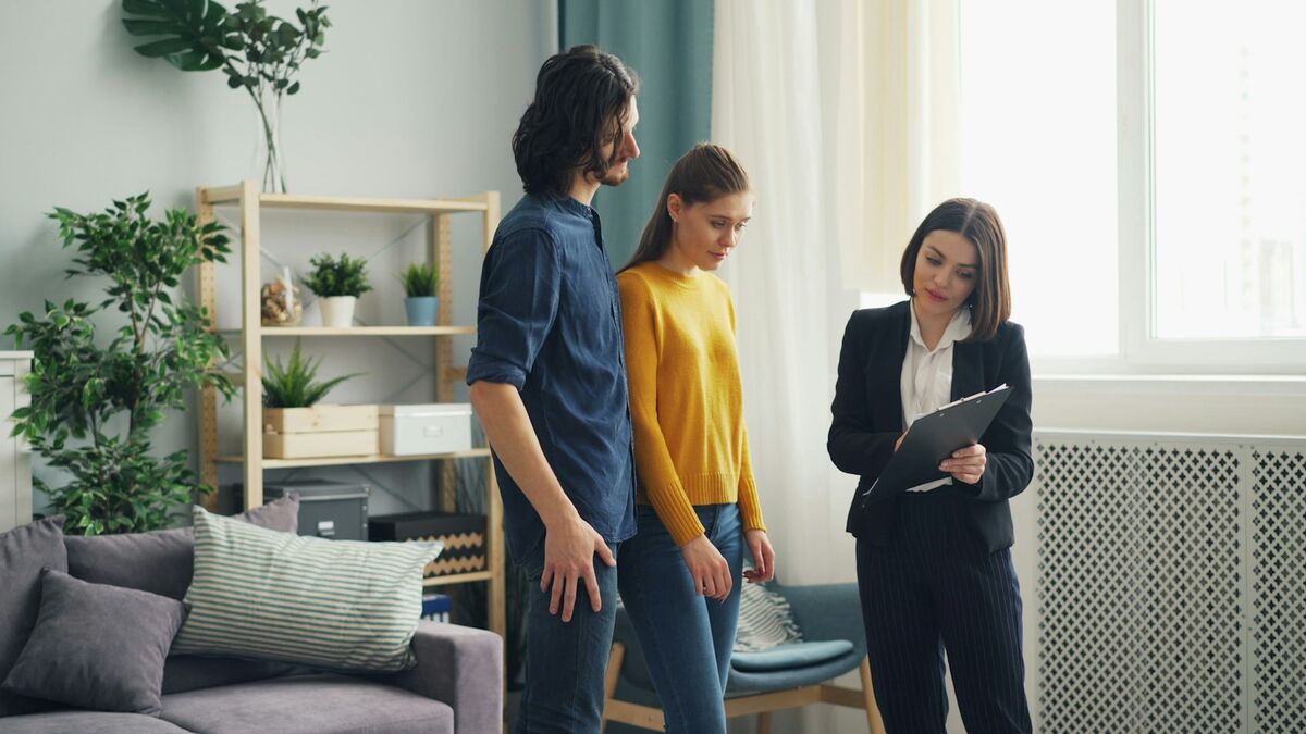 A letting agent with a tablet showing a flat to a couple